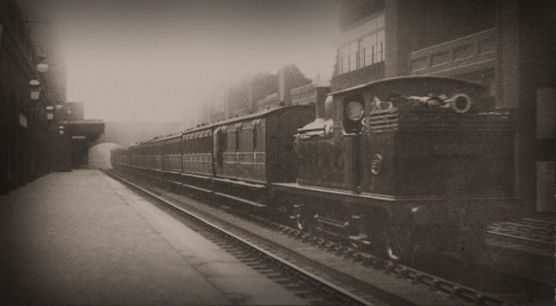 No. 577 from series A62 of 1907 passes Bishopsgate Low Level station on the 1.45pm Liverpool Street to Albert Dock on 12th May 1912. the train is comprised of an eclectic selection of types and vintages, and the loco is the 'wrong way around', usually chimney leading first out of the terminus. Photograph © Public Domain.